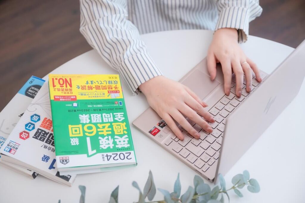 ノートパソコンを操作する手元と英検®1級の参考書