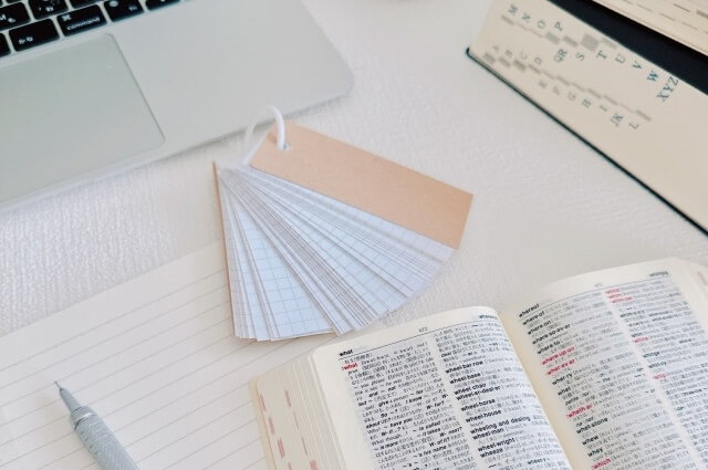 英語の辞書とノートパソコン、単語帳の画像