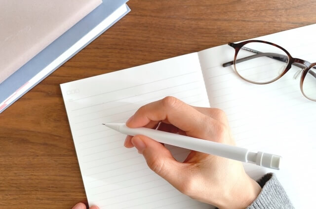 開いたノート、ペンを持つ手元と眼鏡