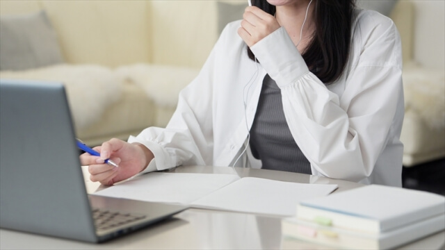 ノートパソコンを開き、ノートを開いて勉強する女性