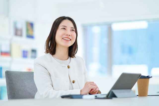タブレットを机に置いた、笑顔の女性の写真